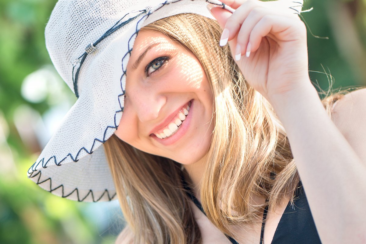 Senior girl poses with hand on hat with only one eye showing. Photo by Justine, photographer in Bismarck ND
